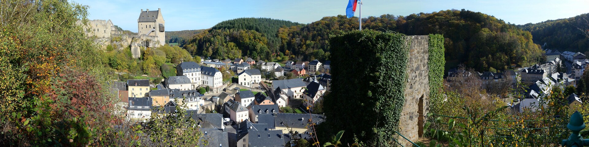 Un pueblo con un castillo, una bandera y una colina con árboles.