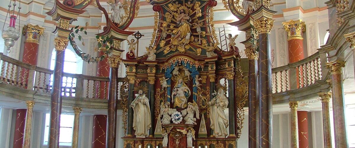 An ornate church interior with a central altar, statues, and a vaulted ceiling.