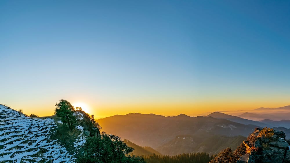 Eine gebirgige Landschaft bei Sonnenaufgang oder Sonnenuntergang, mit wolkenlosem Himmel.