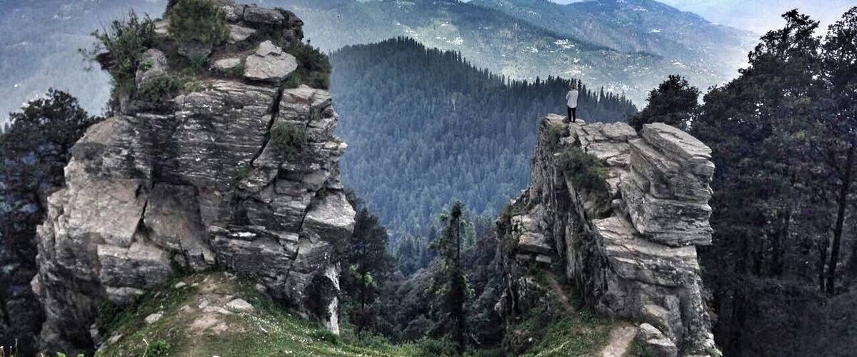 A mountainous landscape with rocky formations and a forested valley.