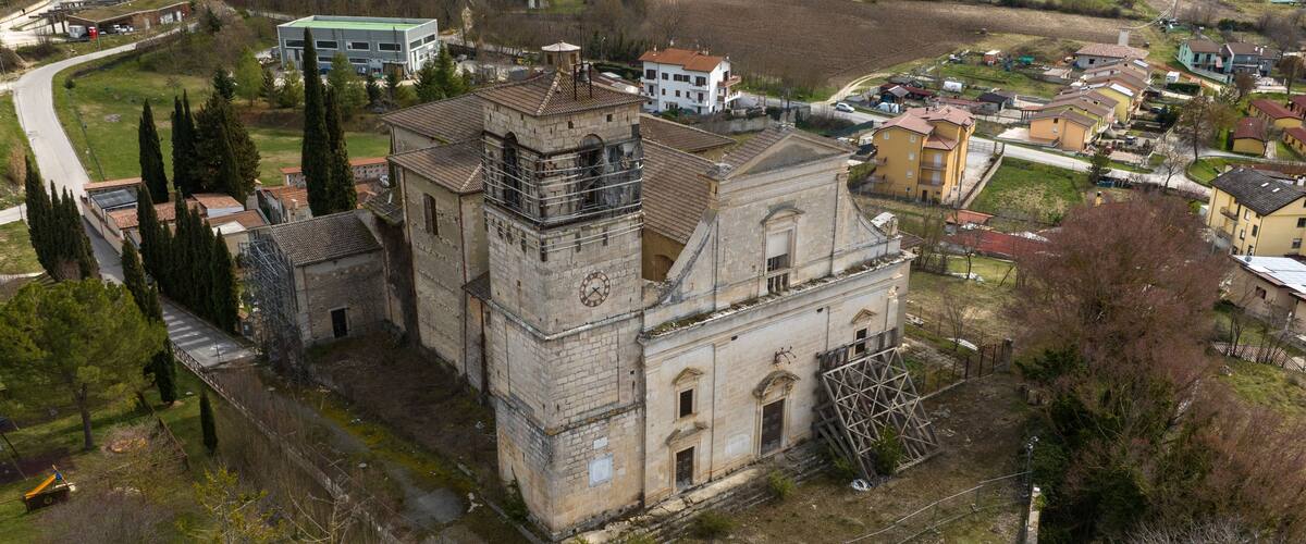 An old church with a clock tower, surrounded by a small village and fields.