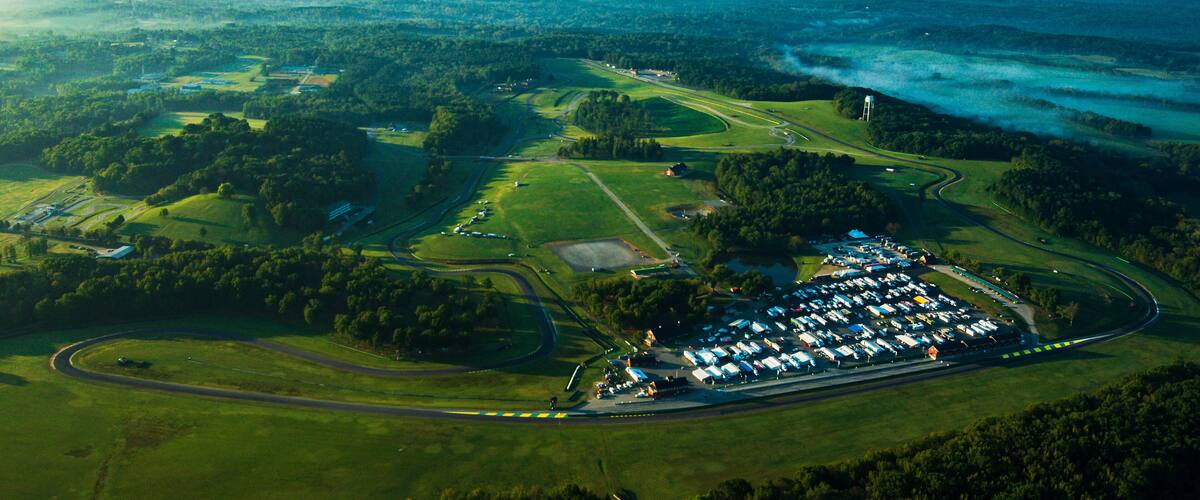 An aerial view of a large parking lot surrounded by green fields and a highway.