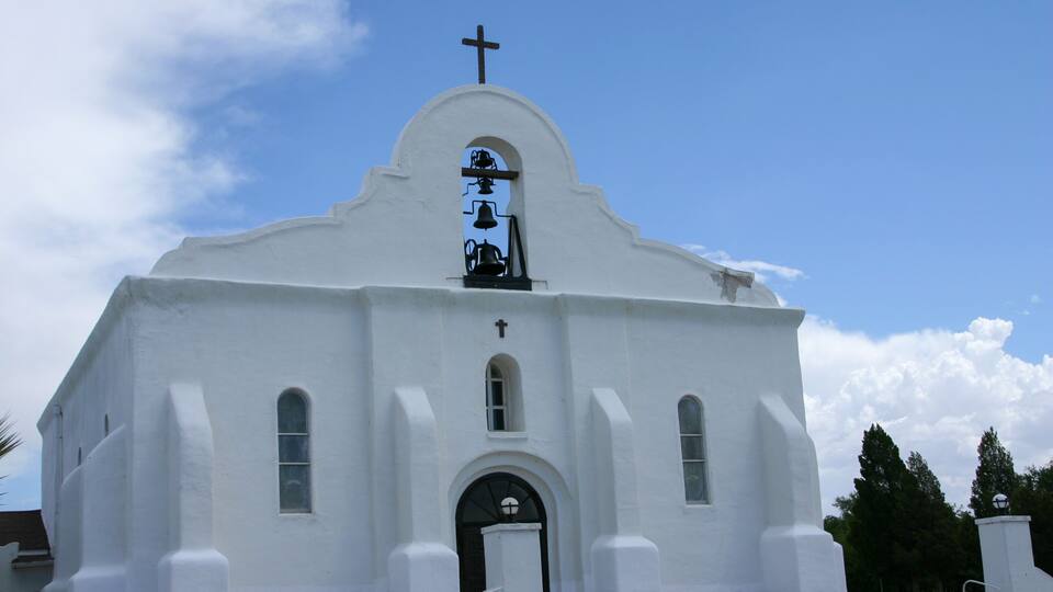 A white church with a cross on top, a bell tower, and a clear blue sky.