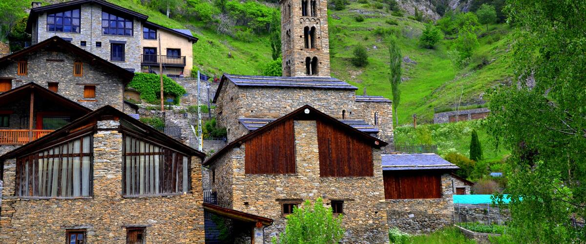 A village with stone buildings, a church tower, and lush green hills.