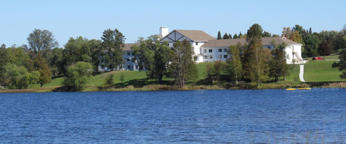 A large white house by a lake with a clear blue sky.