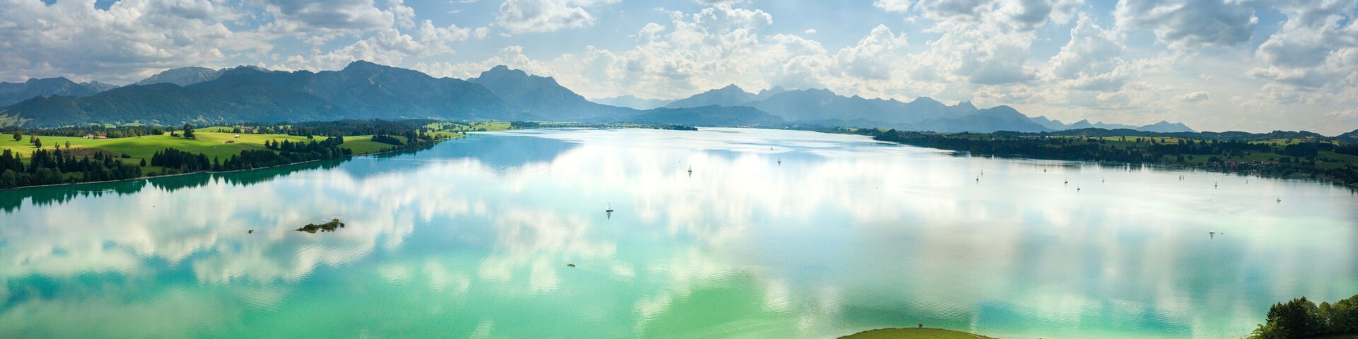 Um lago tranquilo com reflexos nítidos, rodeado por montanhas e uma margem gramada.