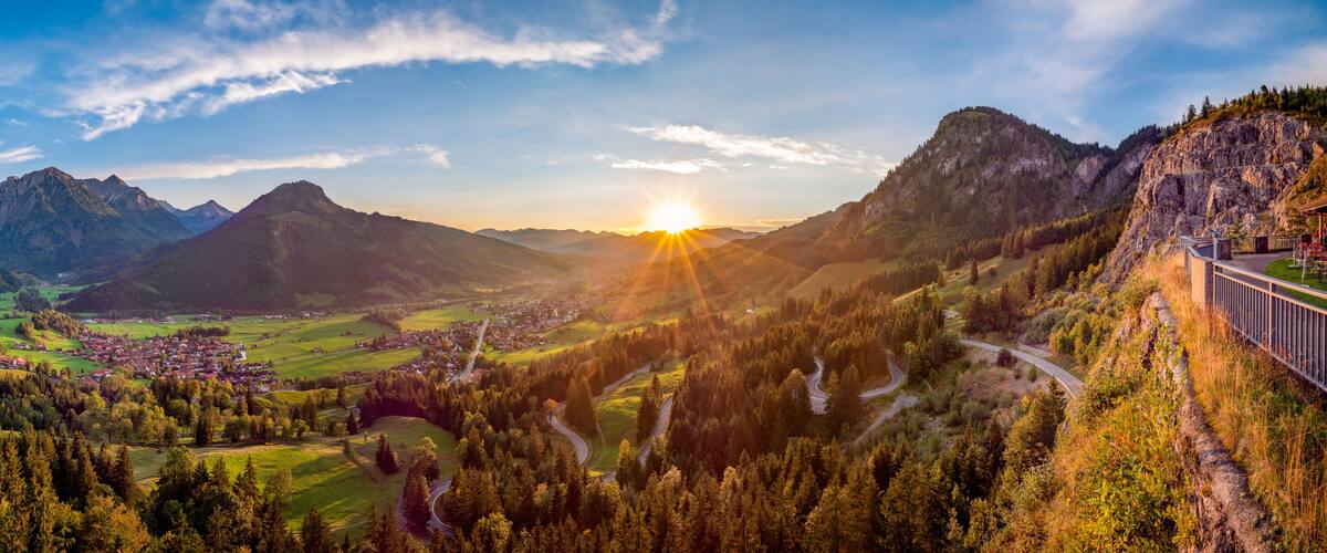 A mountainous landscape with a valley, a winding road, and a bridge.