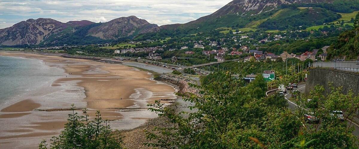 A coastal landscape with a beach, a road, and a mountain range.