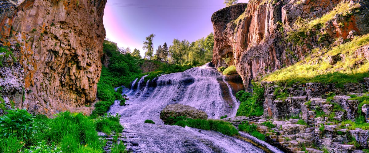 A waterfall cascading down a rocky cliff surrounded by lush greenery.