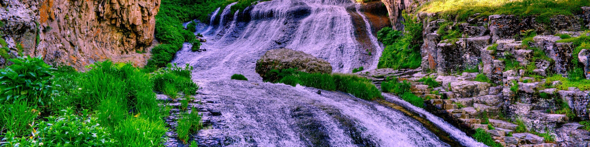 Una cascada se precipita por un acantilado rocoso, rodeada de vegetación exuberante.