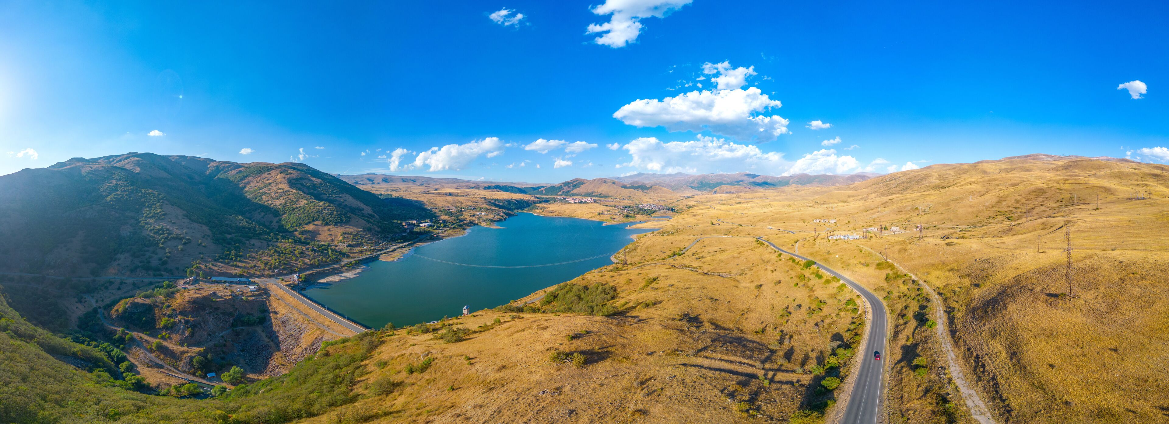 A valley with a lake, mountains, and a winding road.