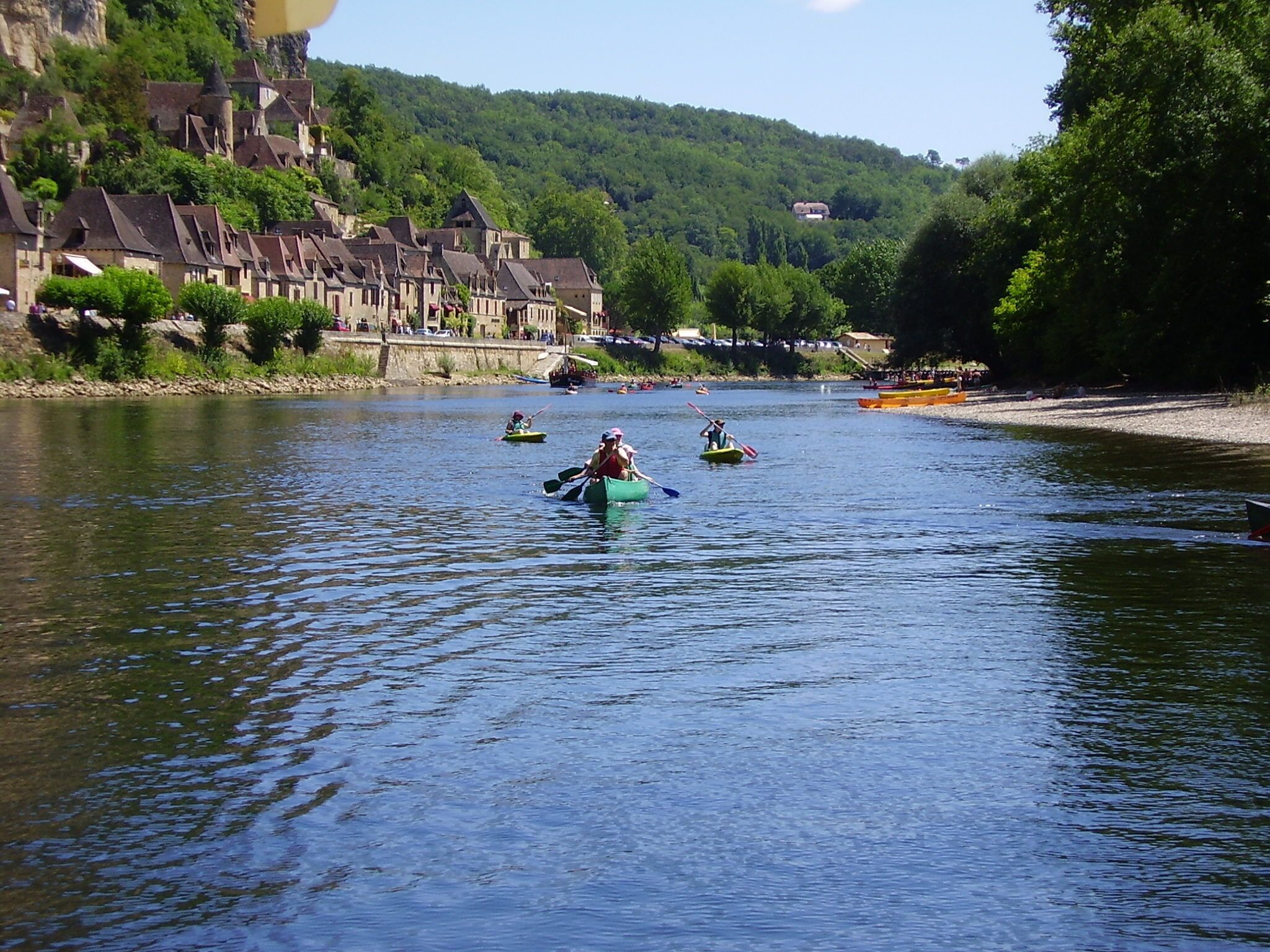 A river with people kayaking. There are houses on a hillside in the background.