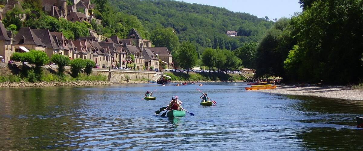 A river with people kayaking. There are houses on a hillside in the background.