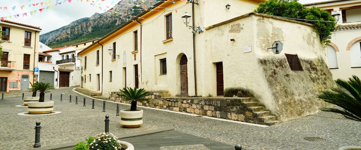 A cobblestone street with historic buildings, a mountain in the background, and colorful flags.