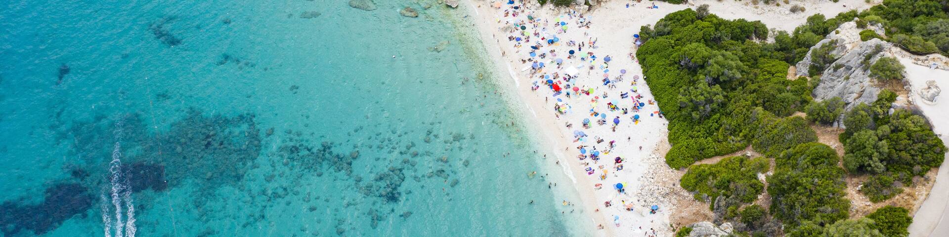 View from above, stunning aerial view of a beautiful beach full of beach umbrellas and people sunbathing and swimming on a turquoise water. Cala Gonone, Sardinia, Italy.