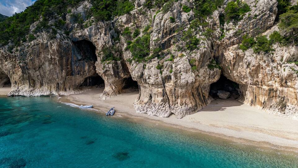 A coastal landscape with rocky cliffs, clear turquoise waters, and a sandy beach with boats.