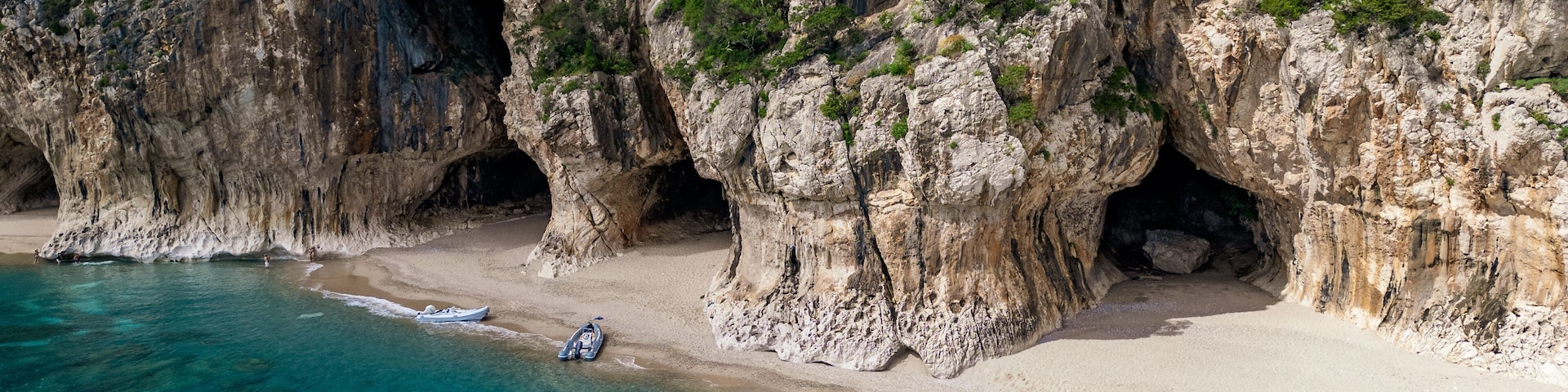Eine KĂŒstenlandschaft mit felsigen Klippen, klarem tĂŒrkisblauem Wasser und einem Sandstrand mit Booten.