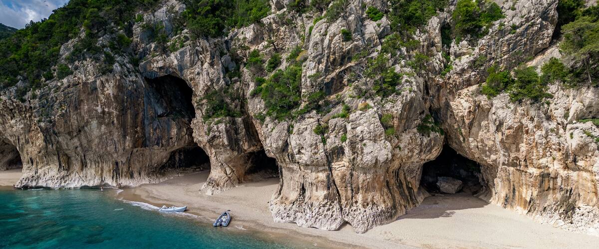 A coastal landscape with rocky cliffs, clear turquoise waters, and a sandy beach with boats.