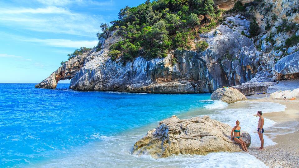 A rocky coastline with clear blue waters and a person standing on a rock.