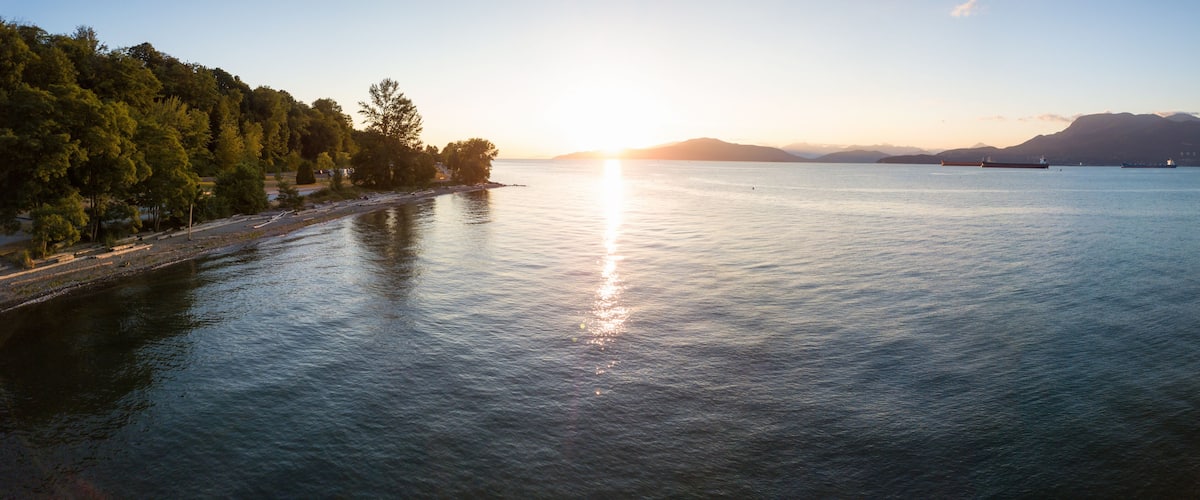 A calm lake at sunset with a forested shore and distant mountains.