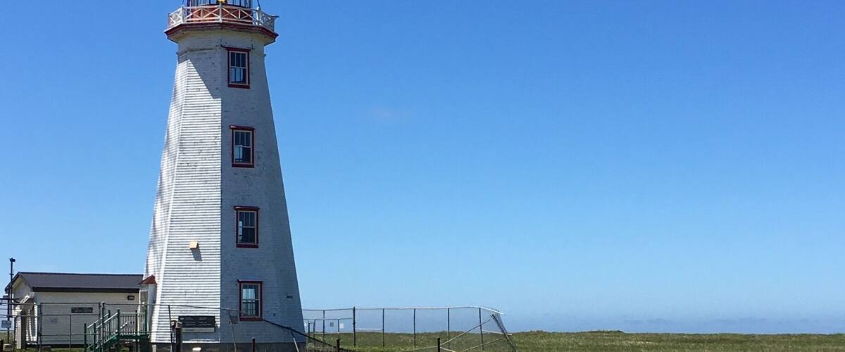 A lighthouse with a red top, a white tower, and a fenced area in front.