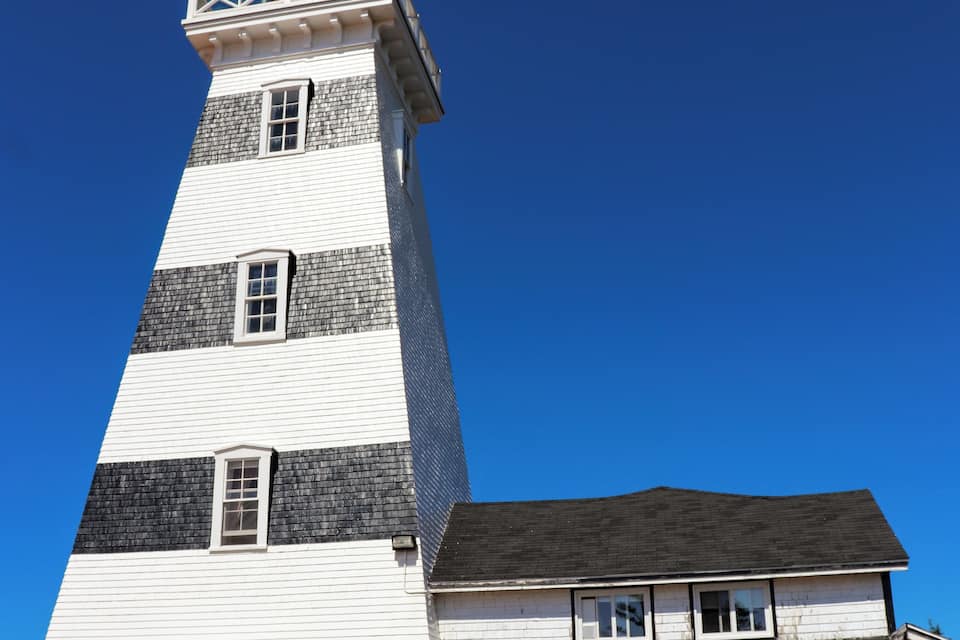 A tall lighthouse with a white and black striped tower and a white base.