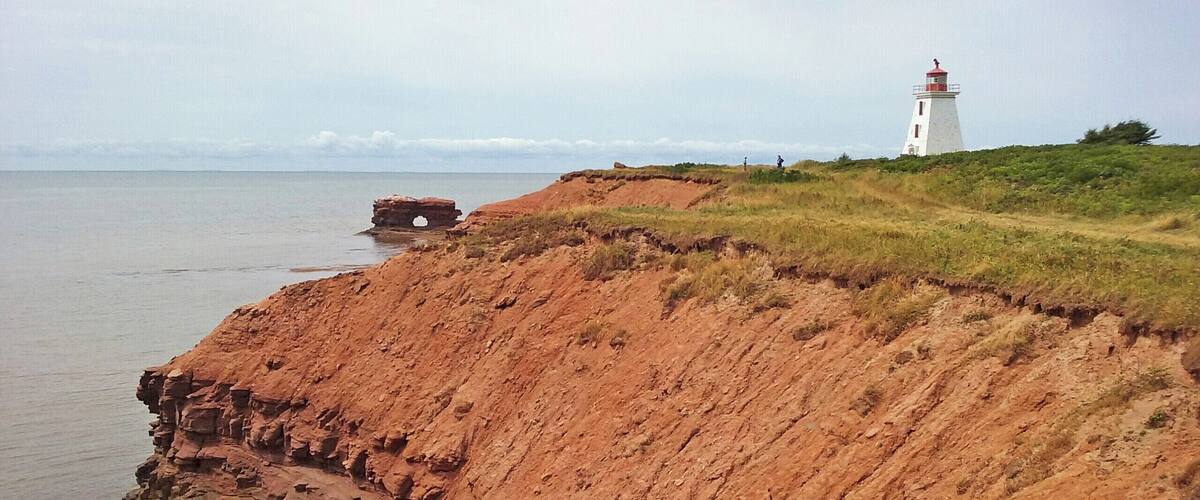 A coastal landscape with a prominent cliff and a lighthouse in the distance.