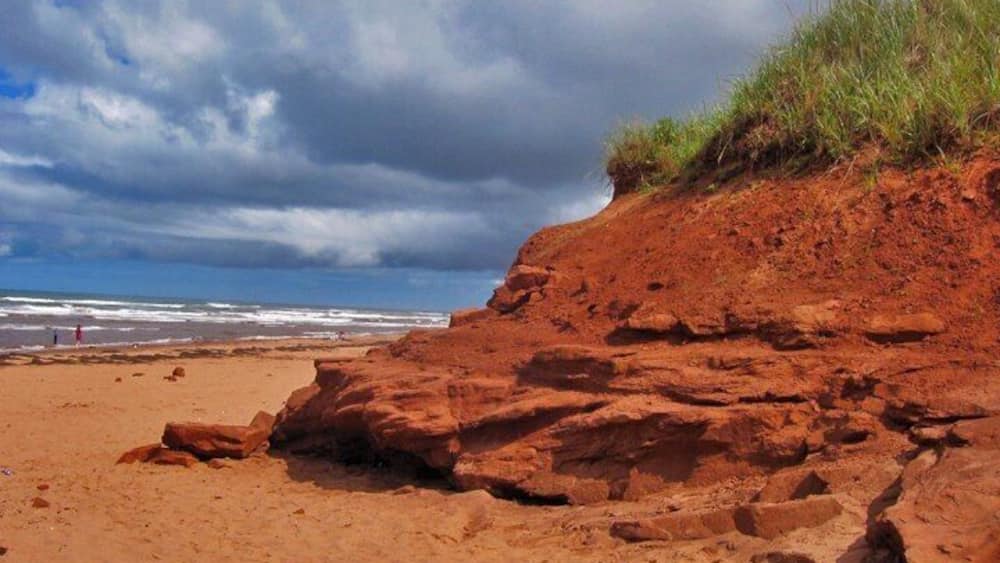 Une plage de sable rouge et une grande formation rocheuse.