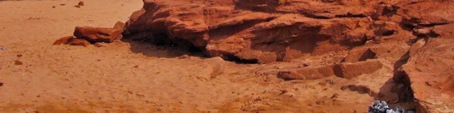 A beach with red sand and a large rock formation.