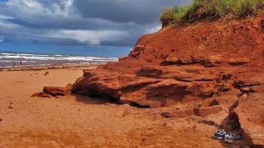 A beach with red sand and a large rock formation.