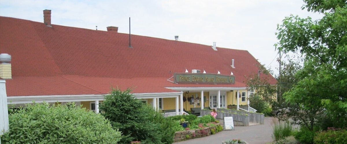 A pathway leading to a yellow building with a red roof, surrounded by lush greenery and yellow flowers.
