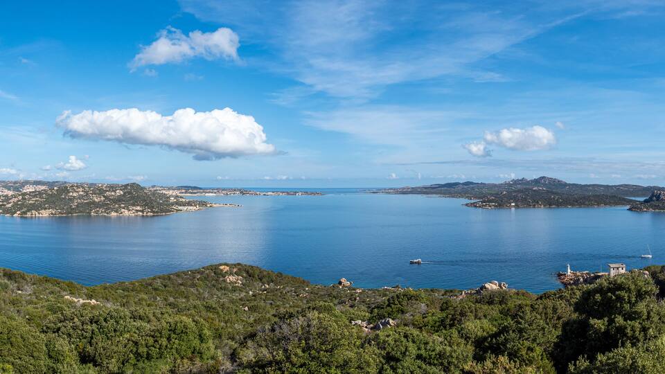 A coastal landscape with a large body of water, rocky islands, and a lighthouse.