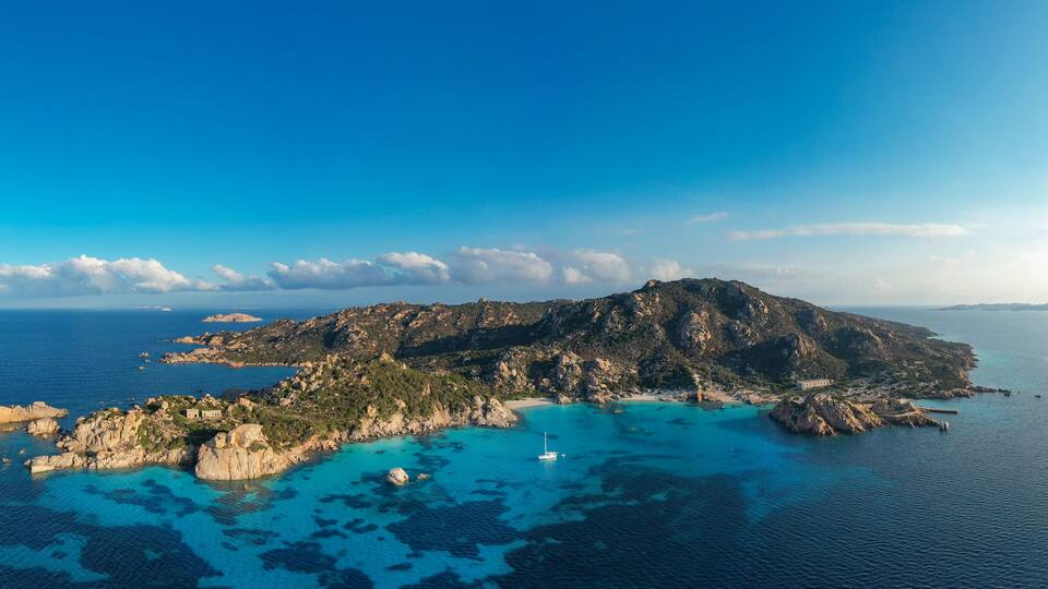 A coastal island with clear turquoise waters, rocky terrain, and a small building.