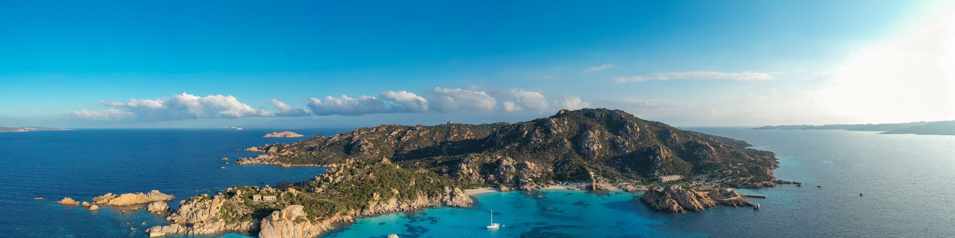 Una isla costera con aguas turquesas cristalinas, terreno rocoso y un pequeño edificio.