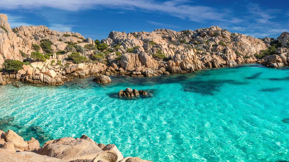 A coastal landscape with clear turquoise waters, rocky cliffs, and a sandy beach.