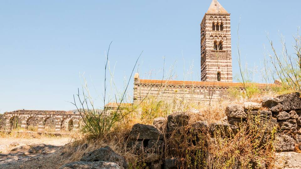 A stone tower with arches and a brick building in the background.