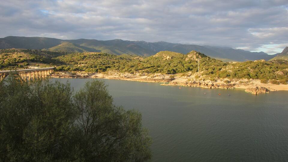 A river with a bridge, surrounded by hills and trees.