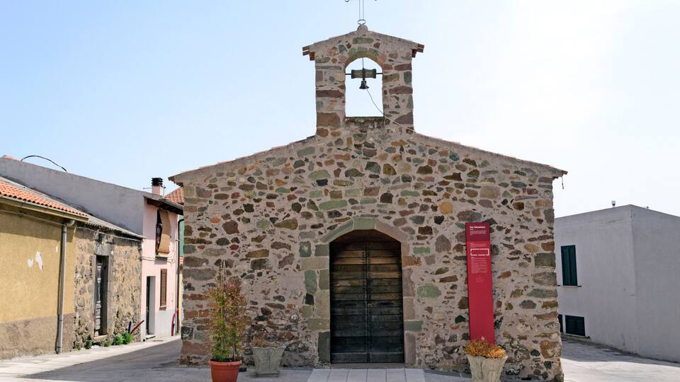 A stone church with a bell tower and a red information board.