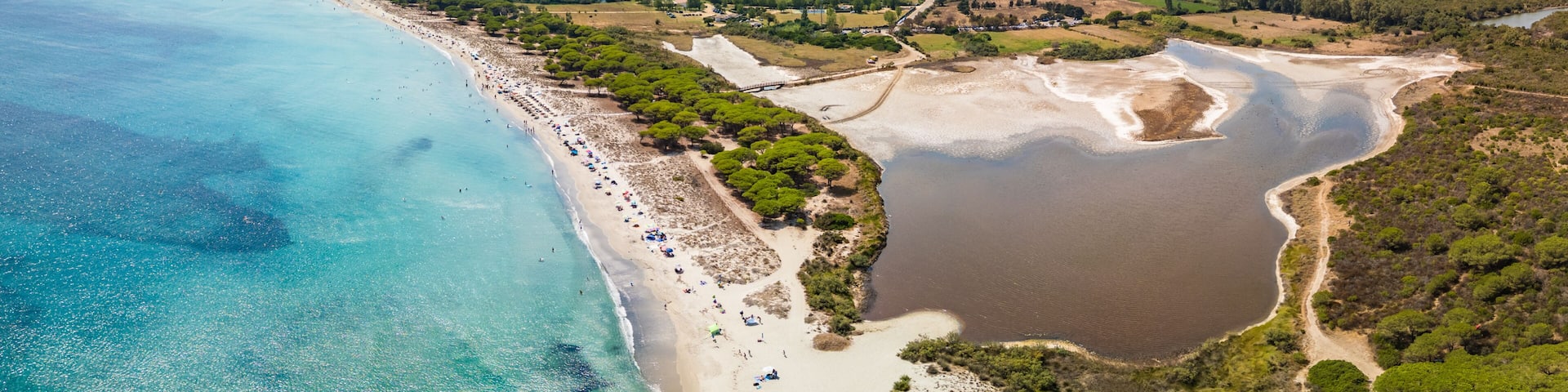 A coastal landscape with a beach, a lake, and a mountainous backdrop.