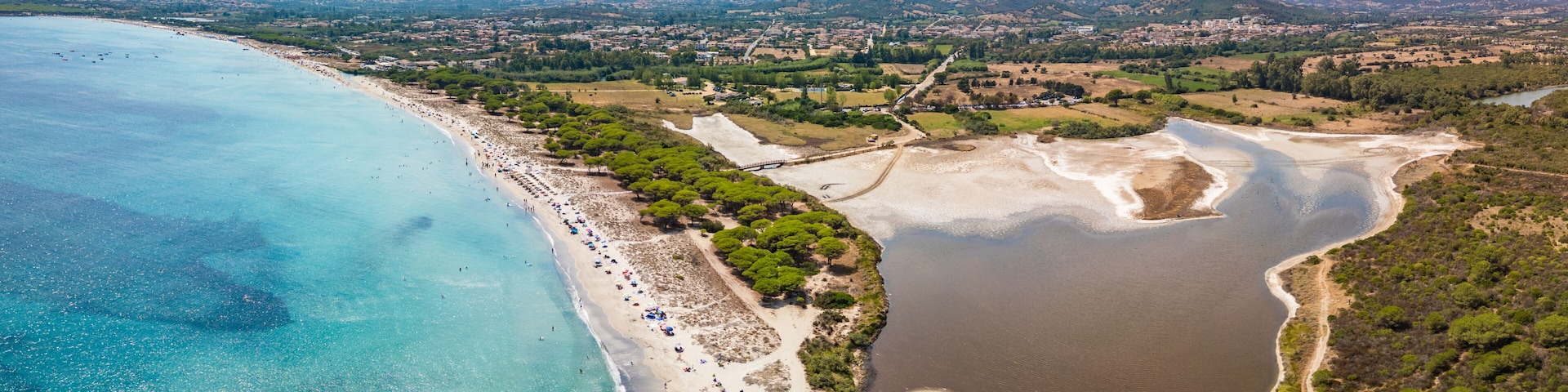 A coastal landscape with a beach, a lake, and a mountainous backdrop.