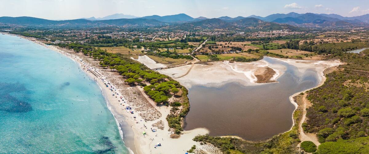 A coastal landscape with a beach, a lake, and a mountainous backdrop.