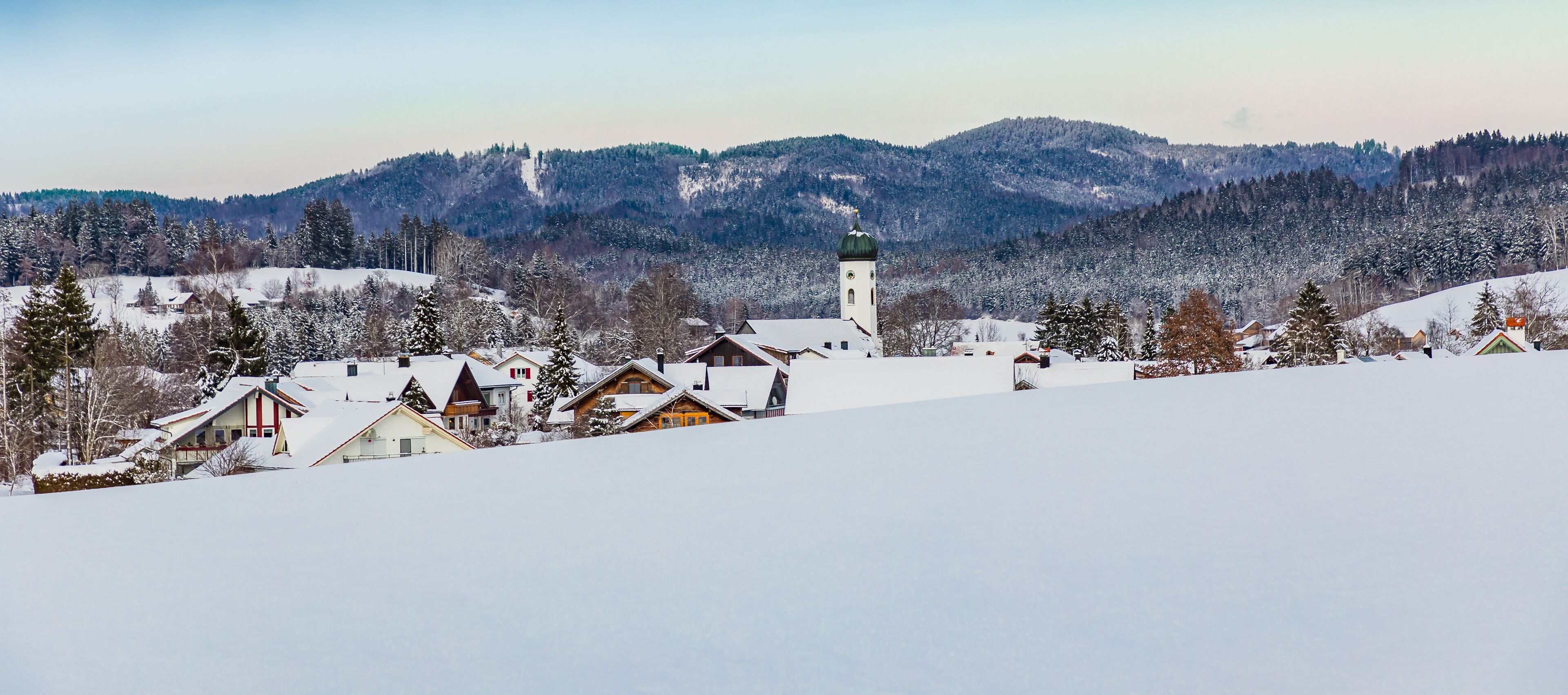 A snow-covered village with houses and a church on a hill.