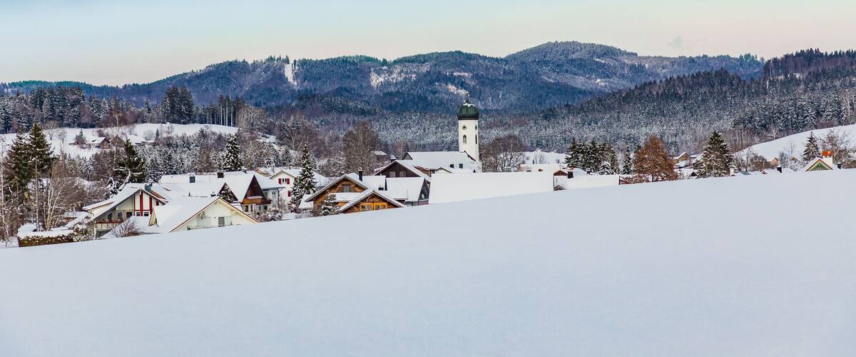 A snow-covered village with houses and a church on a hill.