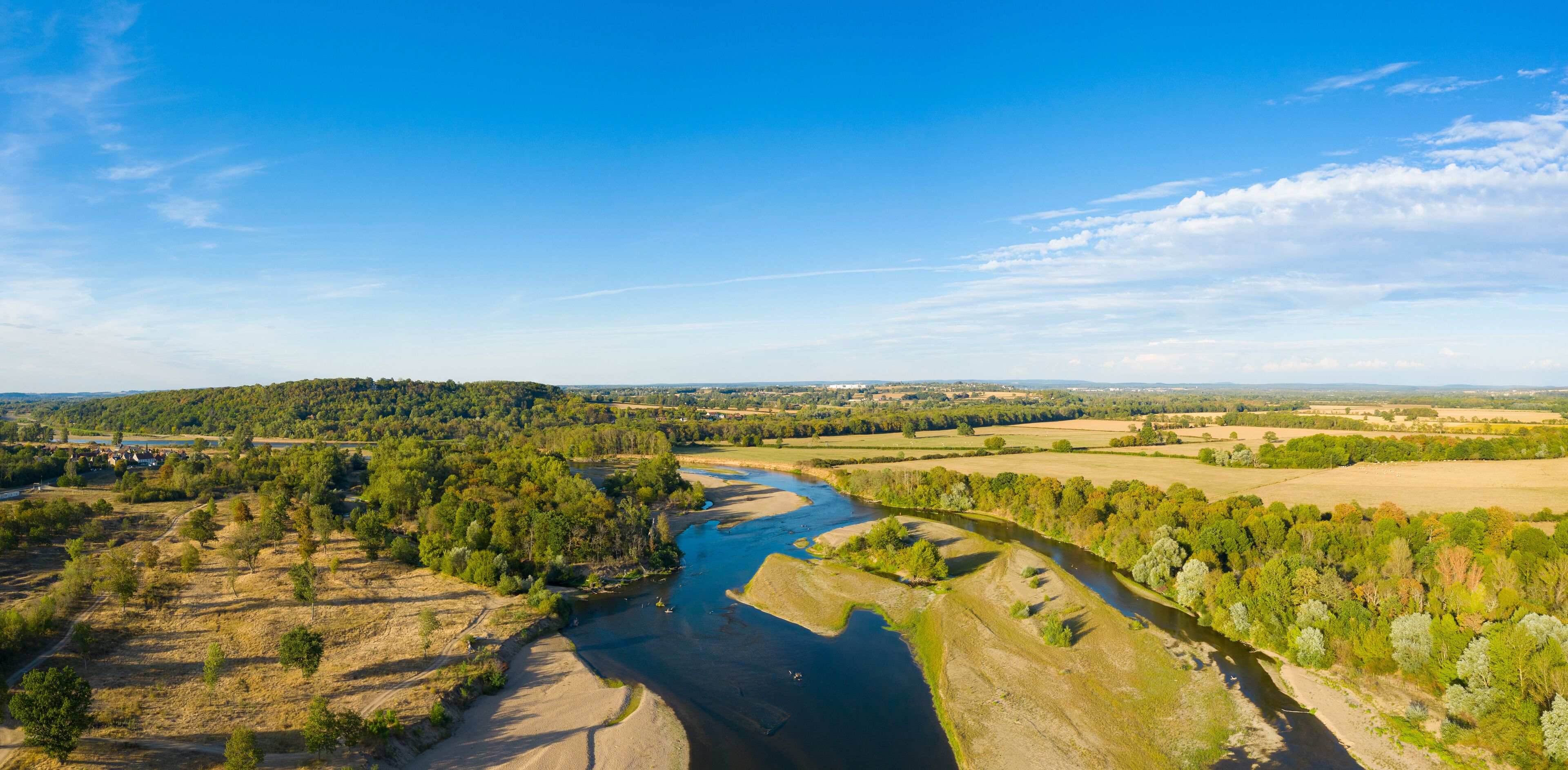 A river winding through a valley with surrounding fields and distant hills.