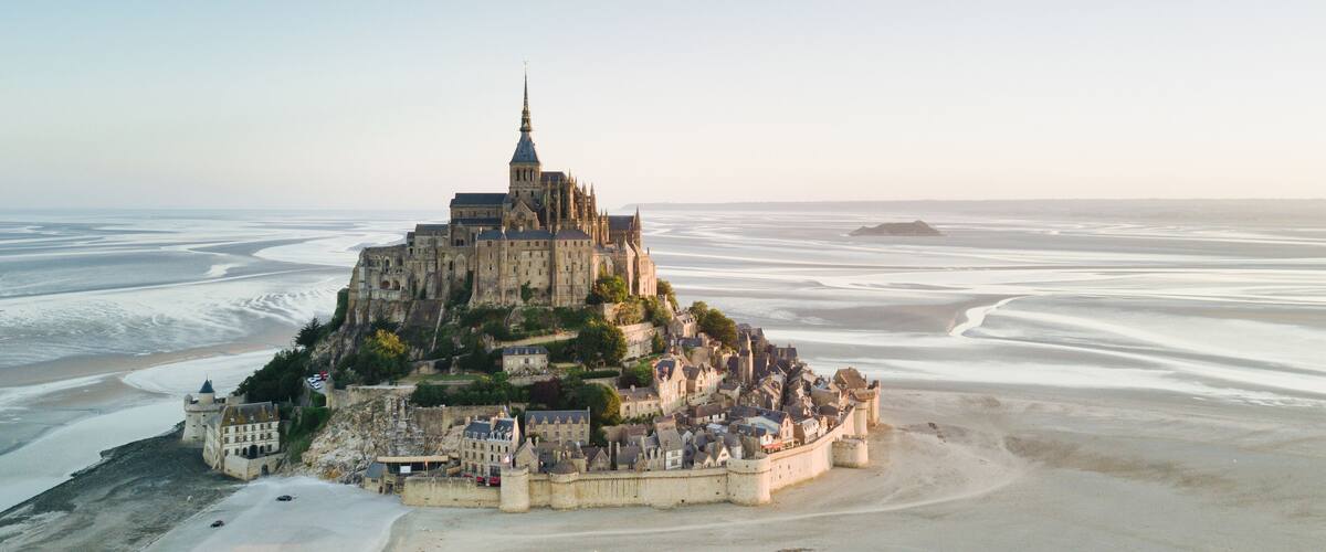 A historic castle on a coastal cliff overlooking a vast beach and calm sea.
