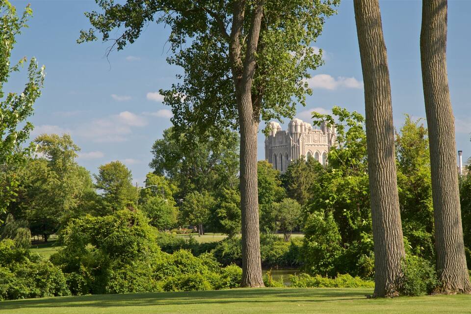 A park with tall trees and a historic building in the background.