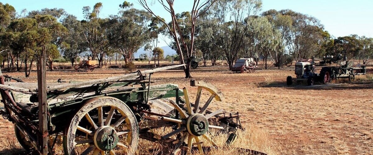 A vintage tractor and a wooden cart in a dry, grassy field with trees in the background.