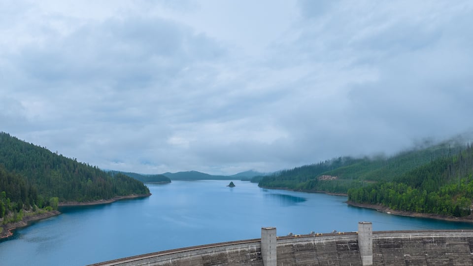 A large dam with a lake surrounded by dense forests and mountains.