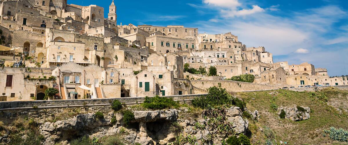 A historic town with ancient stone buildings, a prominent church tower, and a rocky hillside.