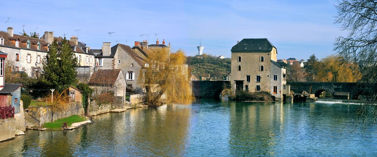 A river with stone buildings and a tower on a hill.
